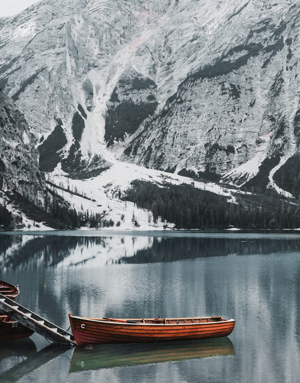 Small boats beneath steep gray mountains beside a lake