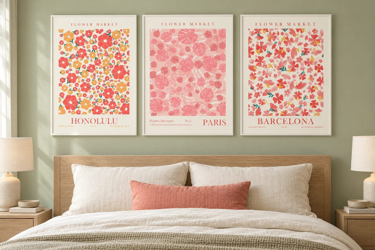 Floral triptych in white frames above a light wood bed against a sage wall.