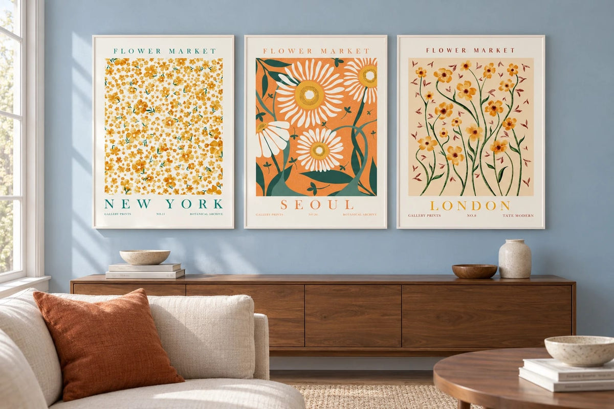 Flower prints above a light sofa on a blue wall with a terracotta cushion.