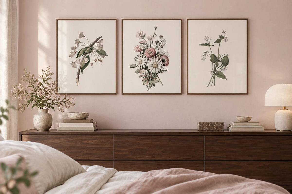 A floral print trio above a dark dresser on a soft pink wall.