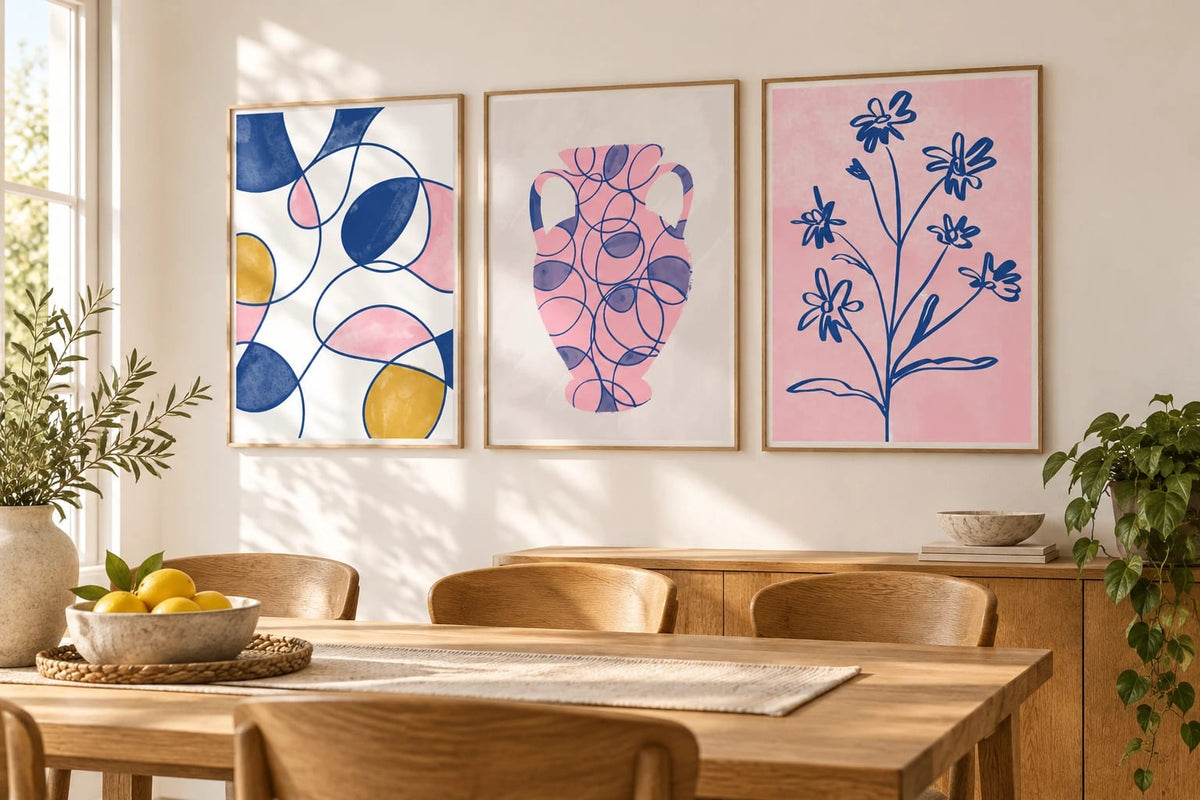 Three colorful prints above a light wood dining table.