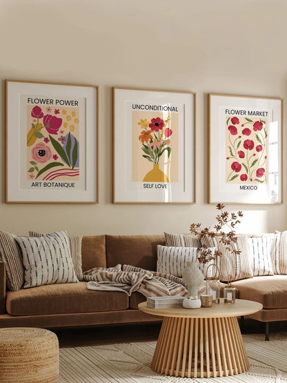 Three floral prints hang above a brown sofa against a beige wall.