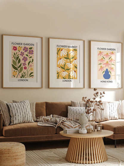 Three floral prints hang above a brown sofa on a beige wall.