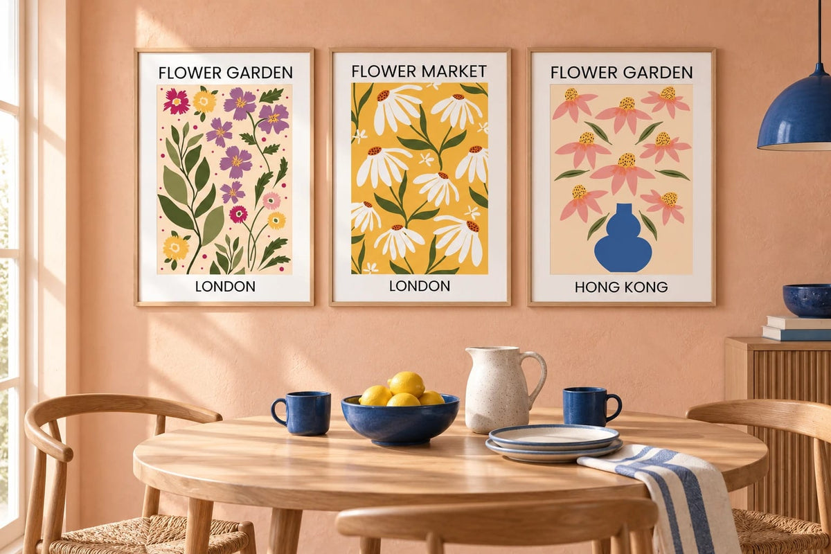 Three floral prints hang on a peach wall above a wood table with blue dishes.