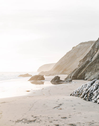 Rocky coastal cliff above a pale sandy shoreline