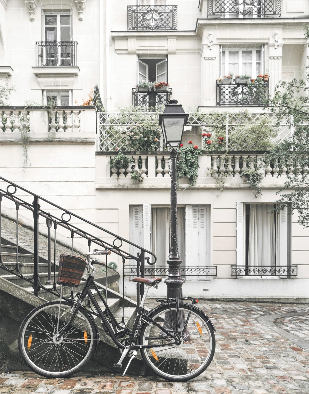 Black bicycle beside a cobbled Paris stair, lamp post, and pale apartment facade