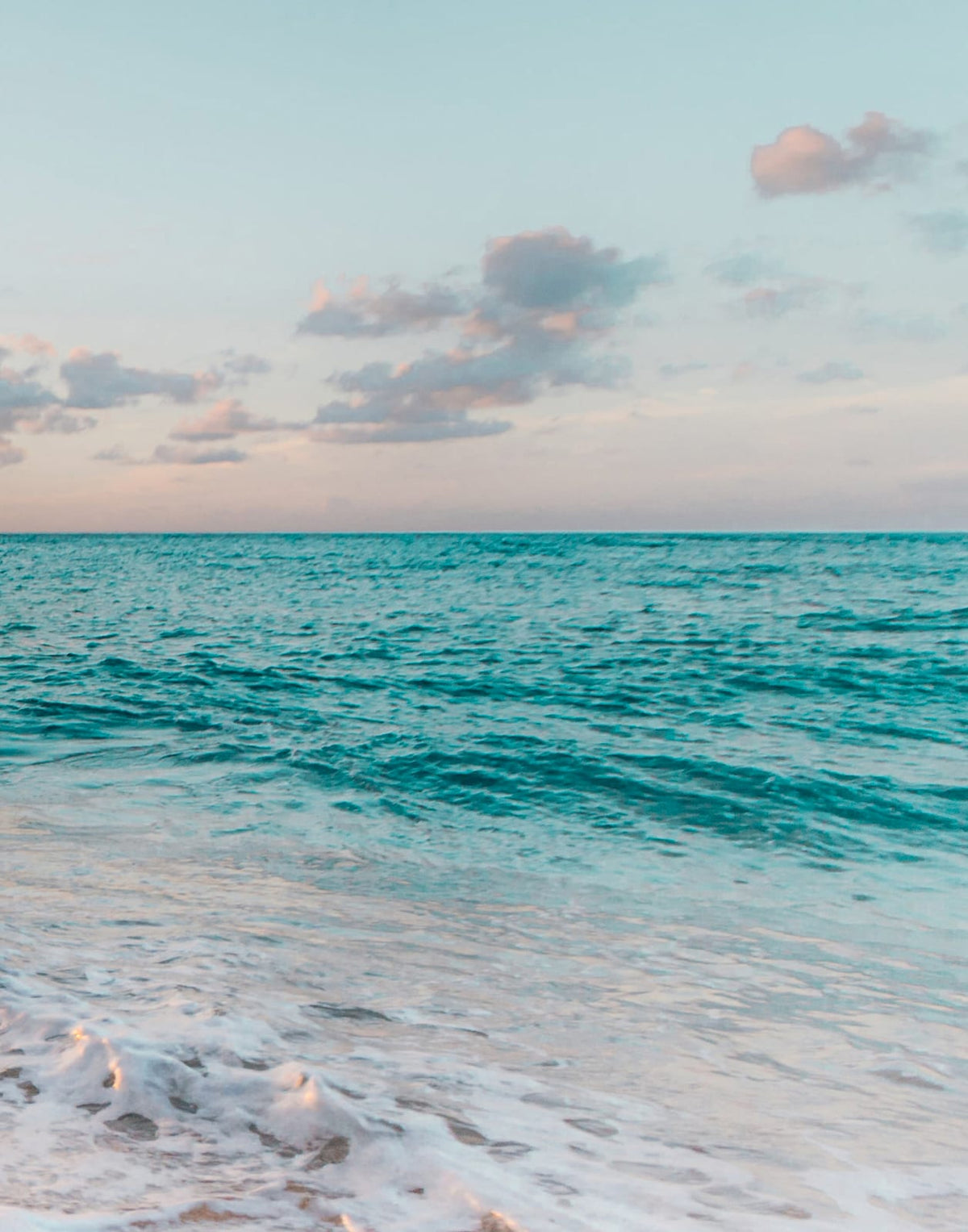 Soft surf crossing peach-lit wet sand at the shoreline