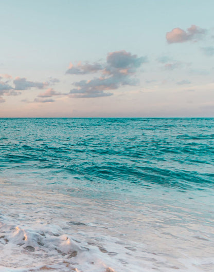 Soft surf crossing peach-lit wet sand at the shoreline
