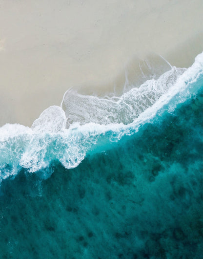 Clear turquoise sea meeting a pale sandy shoreline from above