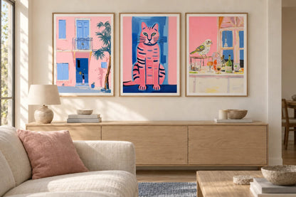 Three prints with a pink facade, striped cat, and bird hang in a warm light living room.