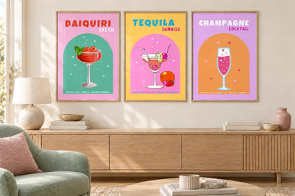 Three cocktail prints hang above a wood cabinet beside a chair.
