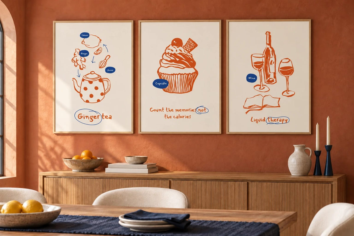 Three food prints hang above a wood sideboard on a terracotta dining room wall.