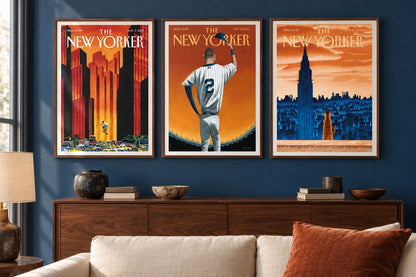 Three orange and blue prints hang above a walnut cabinet on a blue wall.