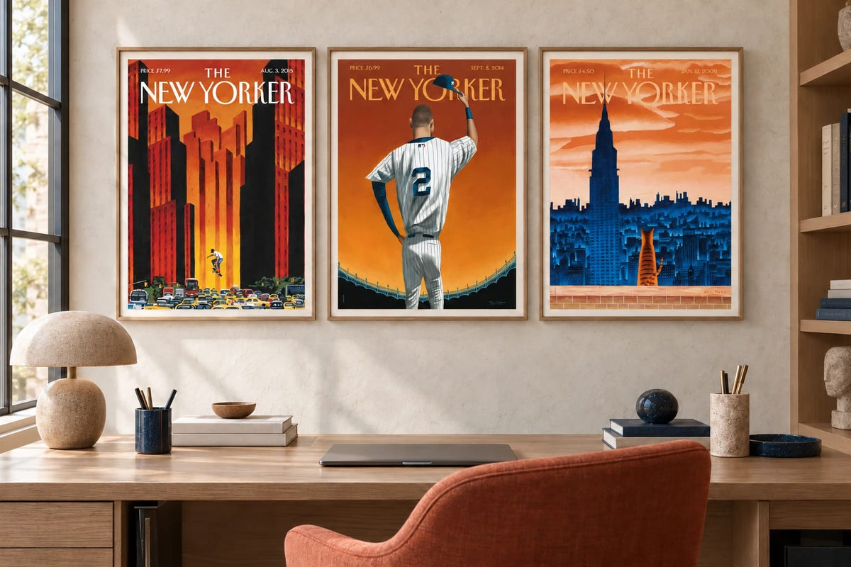 Three orange and blue prints hang above a desk with a beige wall and terracotta chair.