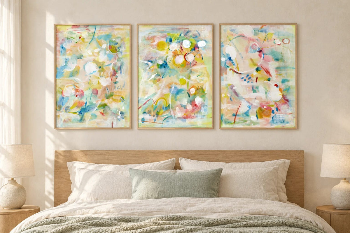 Pastel abstract prints hang over a bed with linen bedding and a sage throw.