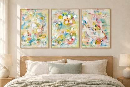 Pastel abstract prints hang over a bed with linen bedding and a sage throw.