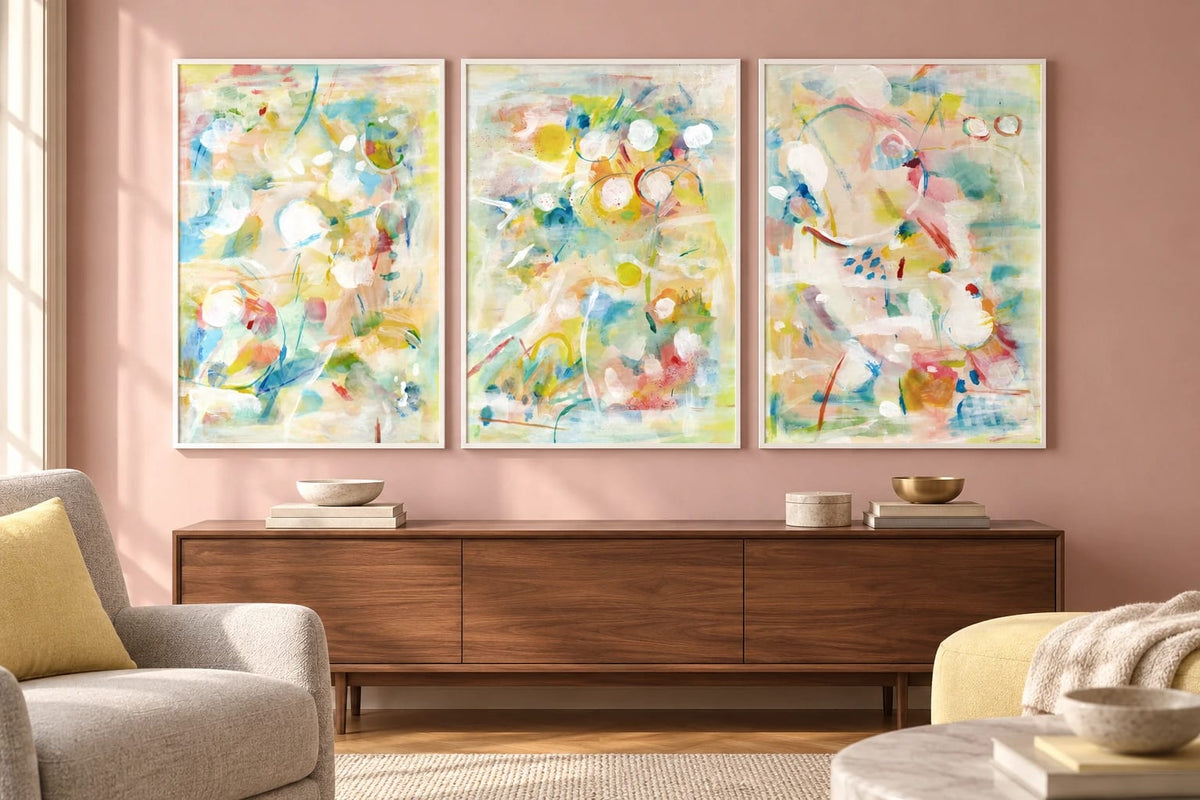 Pastel prints hang on a powder pink wall above a walnut cabinet.