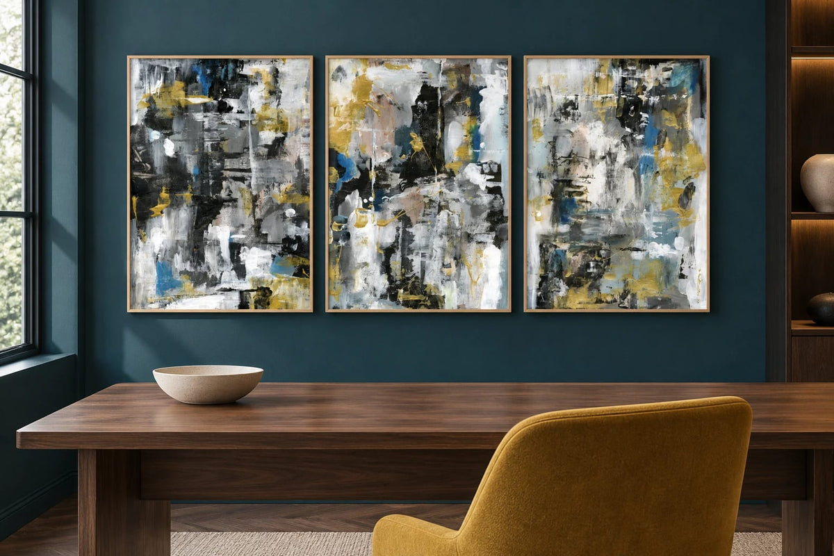 Black and ochre abstract prints hang on a dark teal wall above a wood desk.