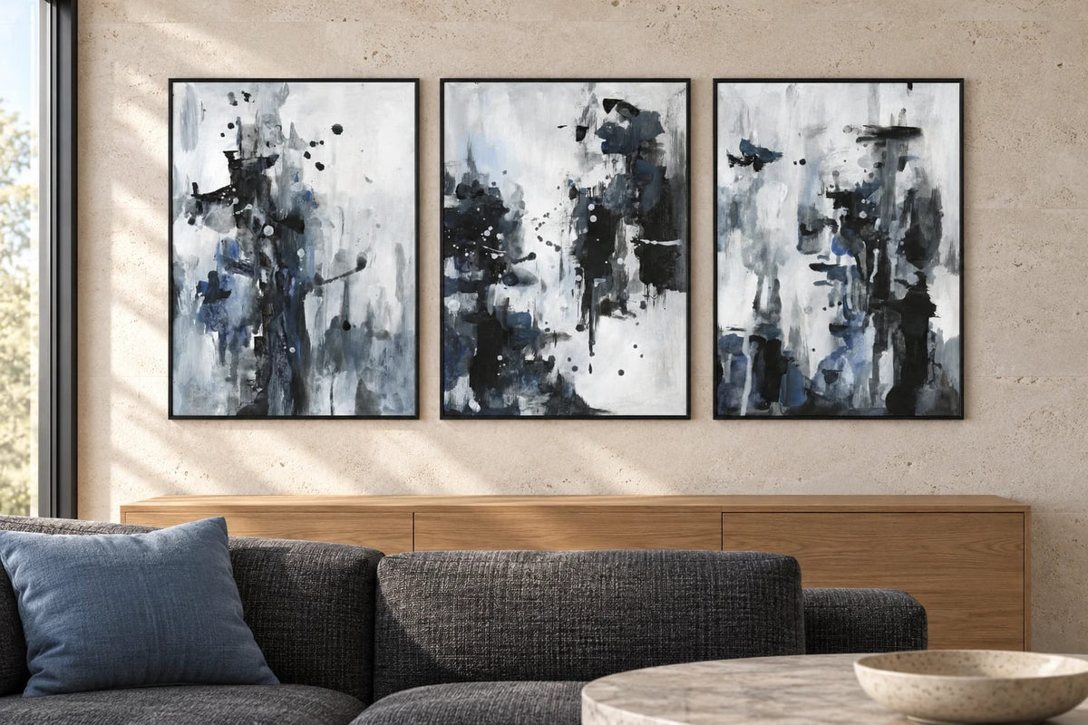Black-gray prints with blue details hang above an oak cabinet and dark sofa.
