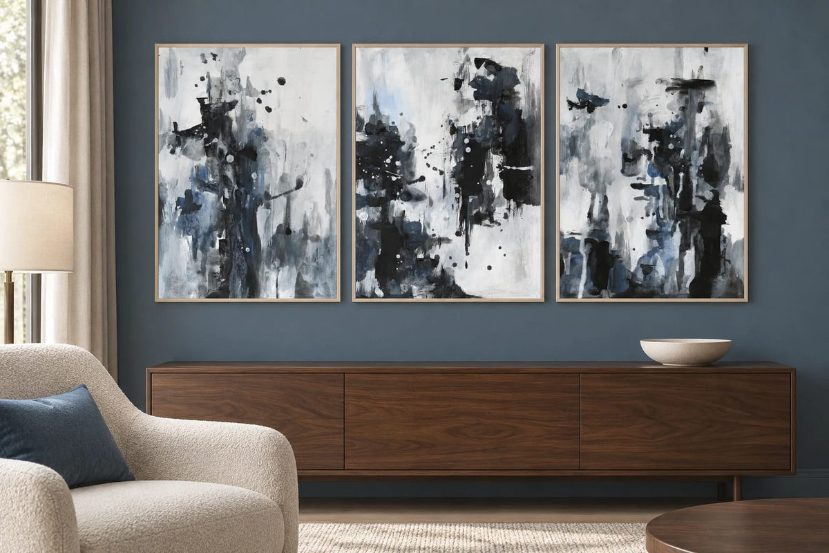 Black-gray prints with blue details hang against a dark blue-gray wall above a walnut cabinet.