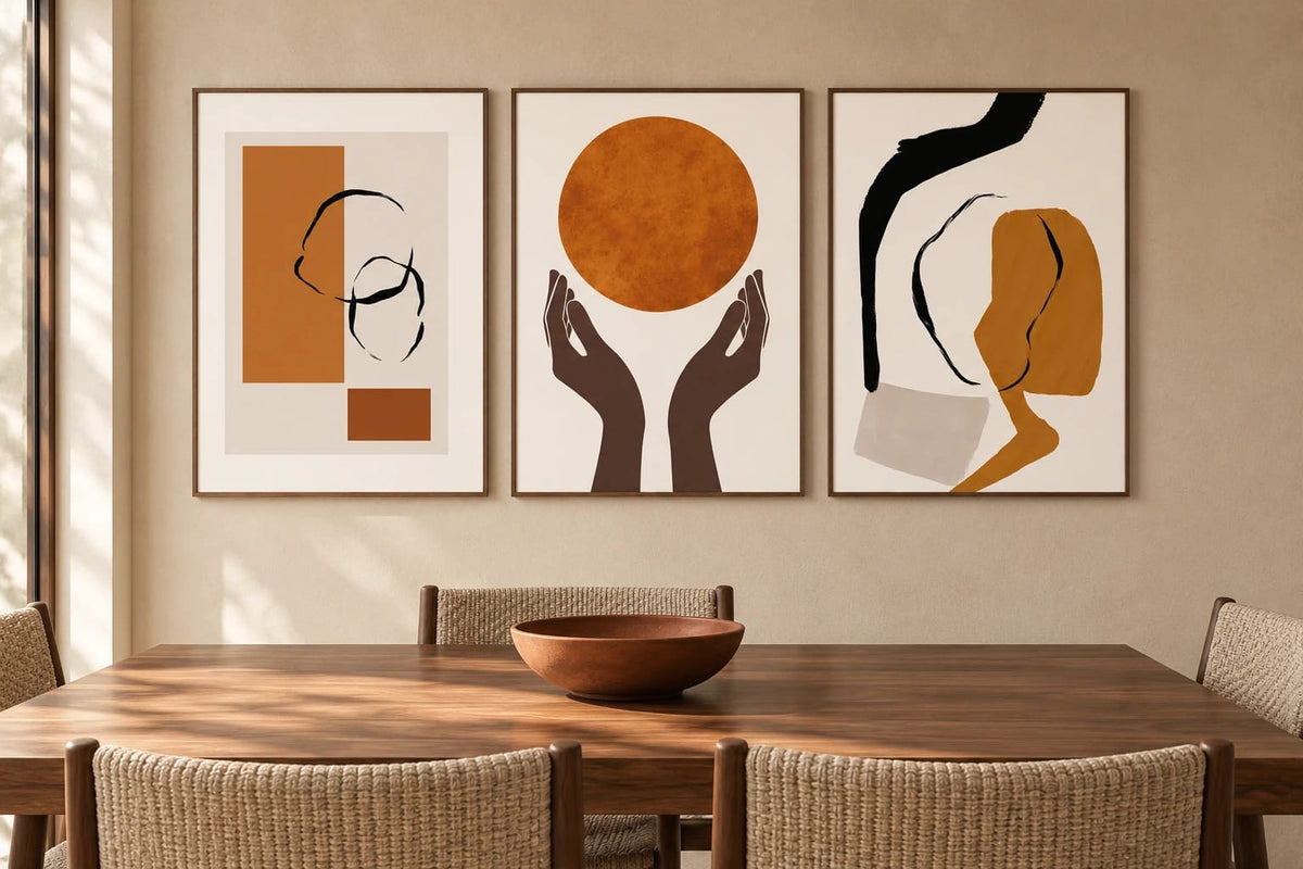 Ochre and black prints above a table with woven chairs on a beige wall.