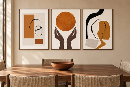 Ochre and black prints above a table with woven chairs on a beige wall.