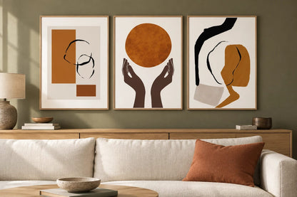 Three ochre and black prints above an oak console near a light sofa on an olive wall.