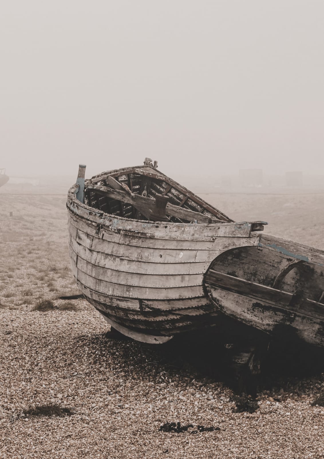 wooden boat on pebbles beside a second boat on a misty shore.