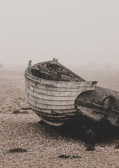 wooden boat on pebbles beside a second boat on a misty shore.