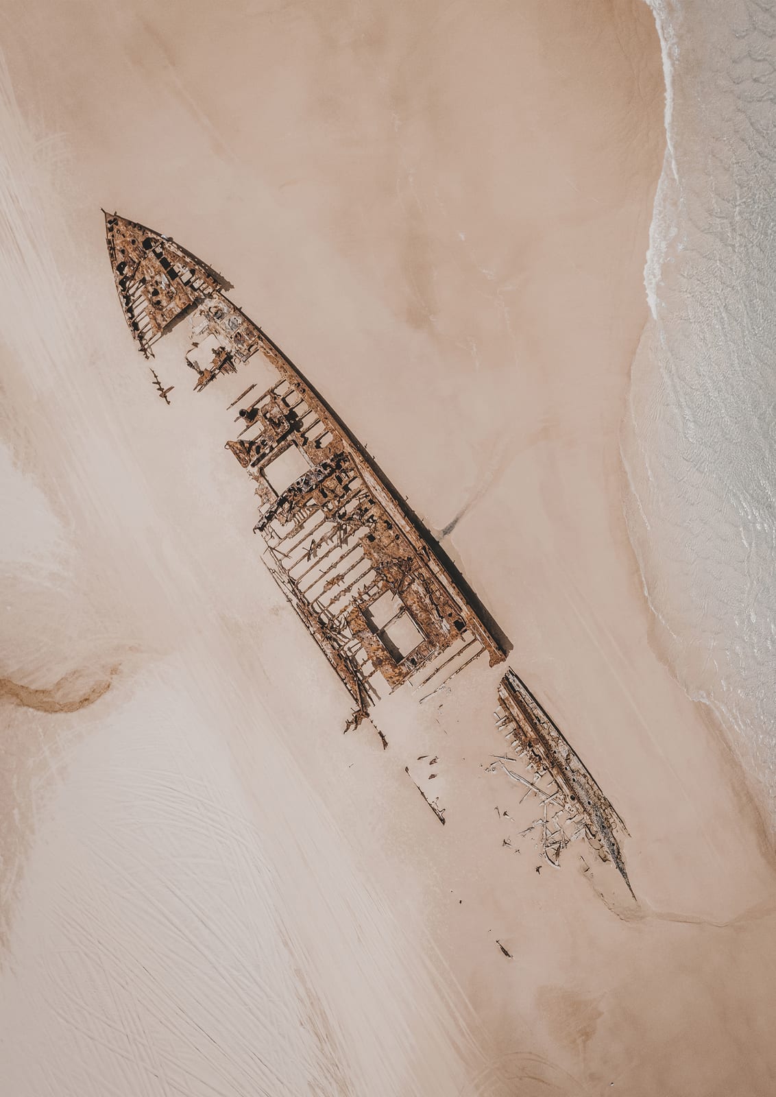 diagonal shipwreck on pale sand beside a thin line of surf.