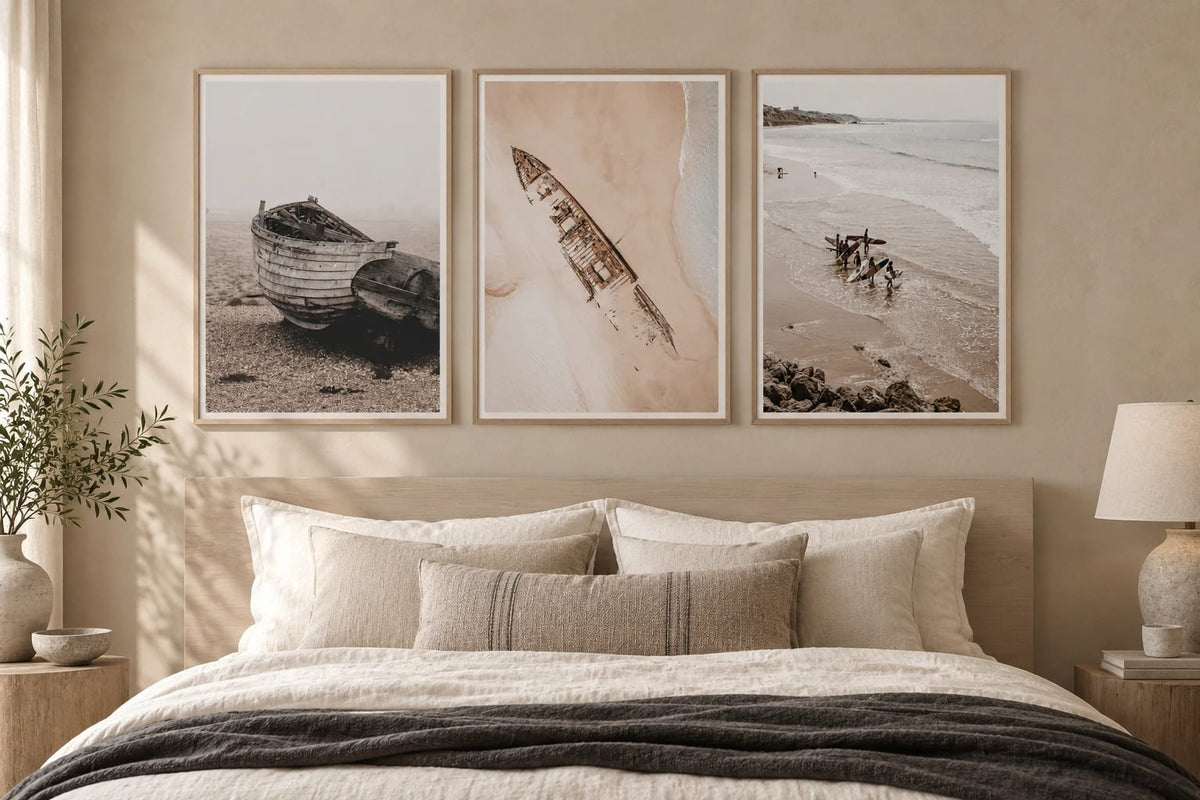 Three shore scenes above a bed in a beige bedroom.