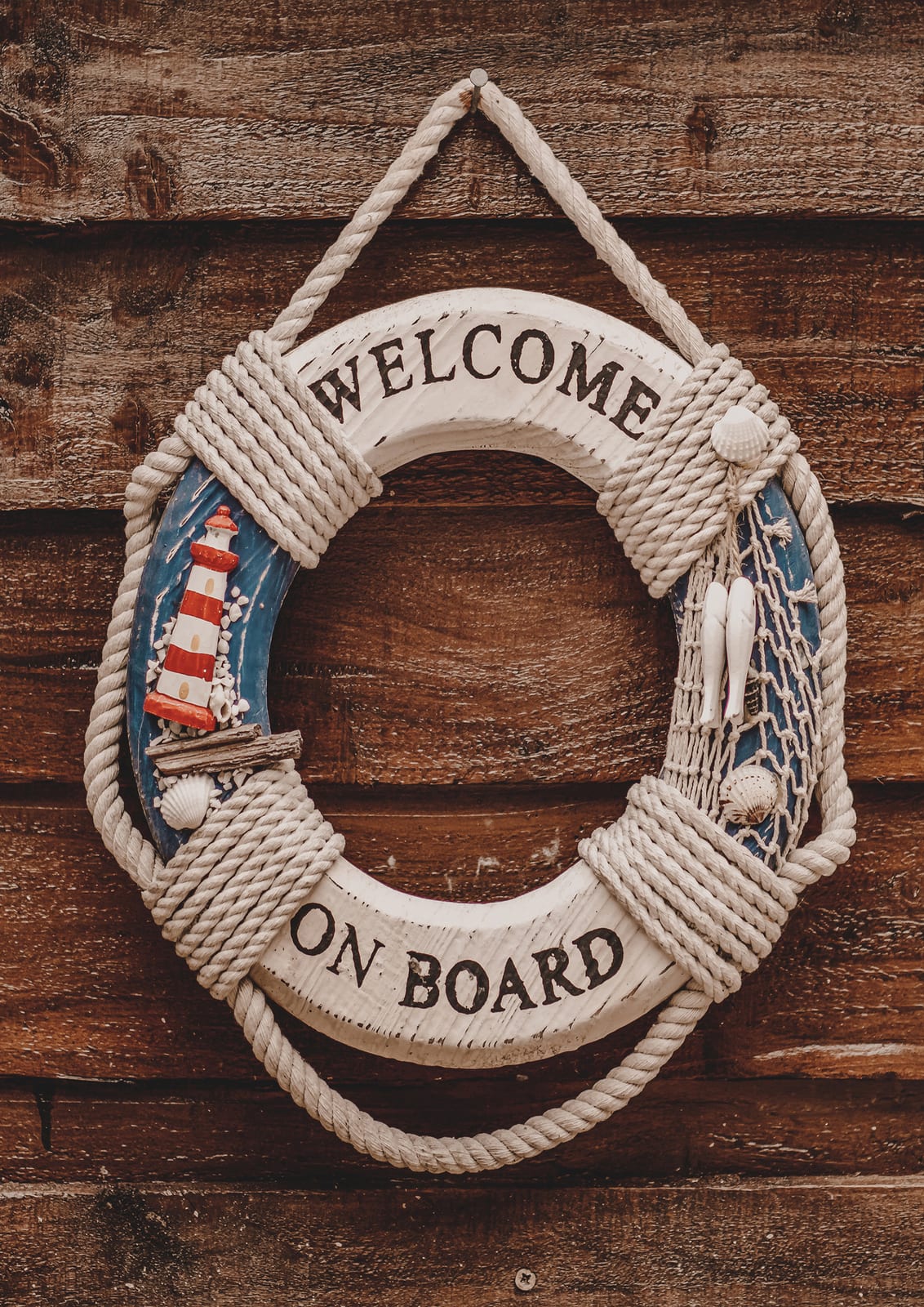 white lifebuoy on wood with rope, small lighthouse, and WELCOME ON BOARD.