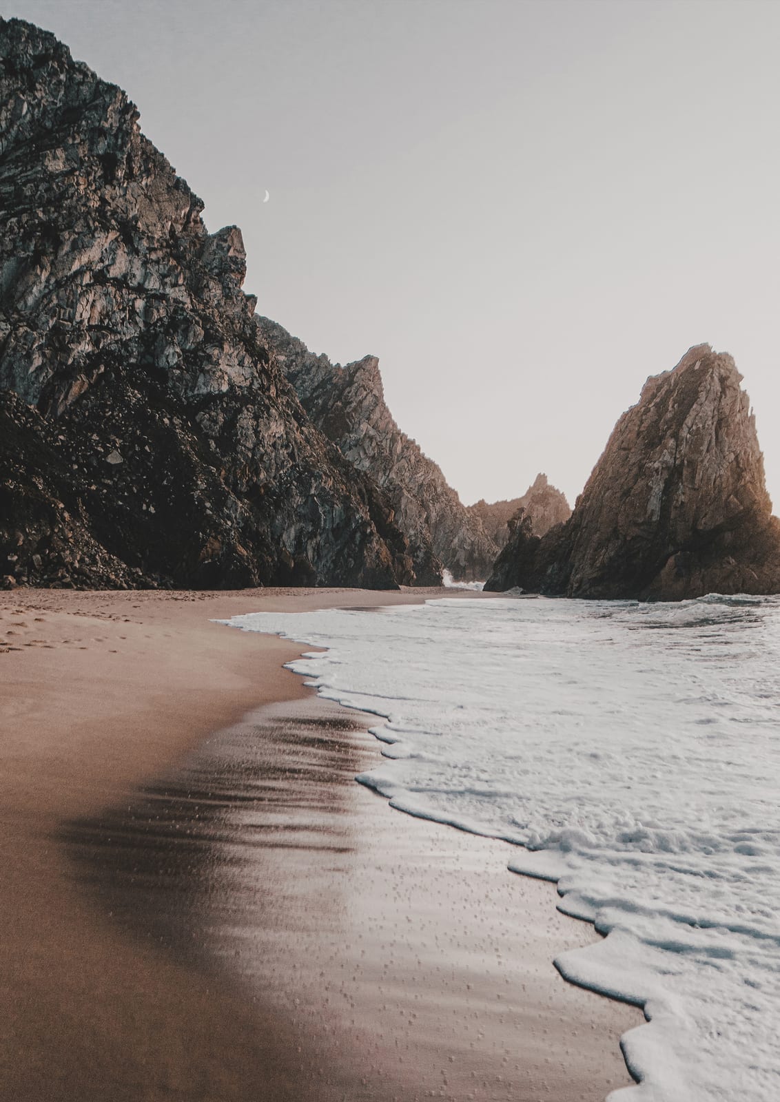 rocky cove with wet sand and white surf between gray cliffs.