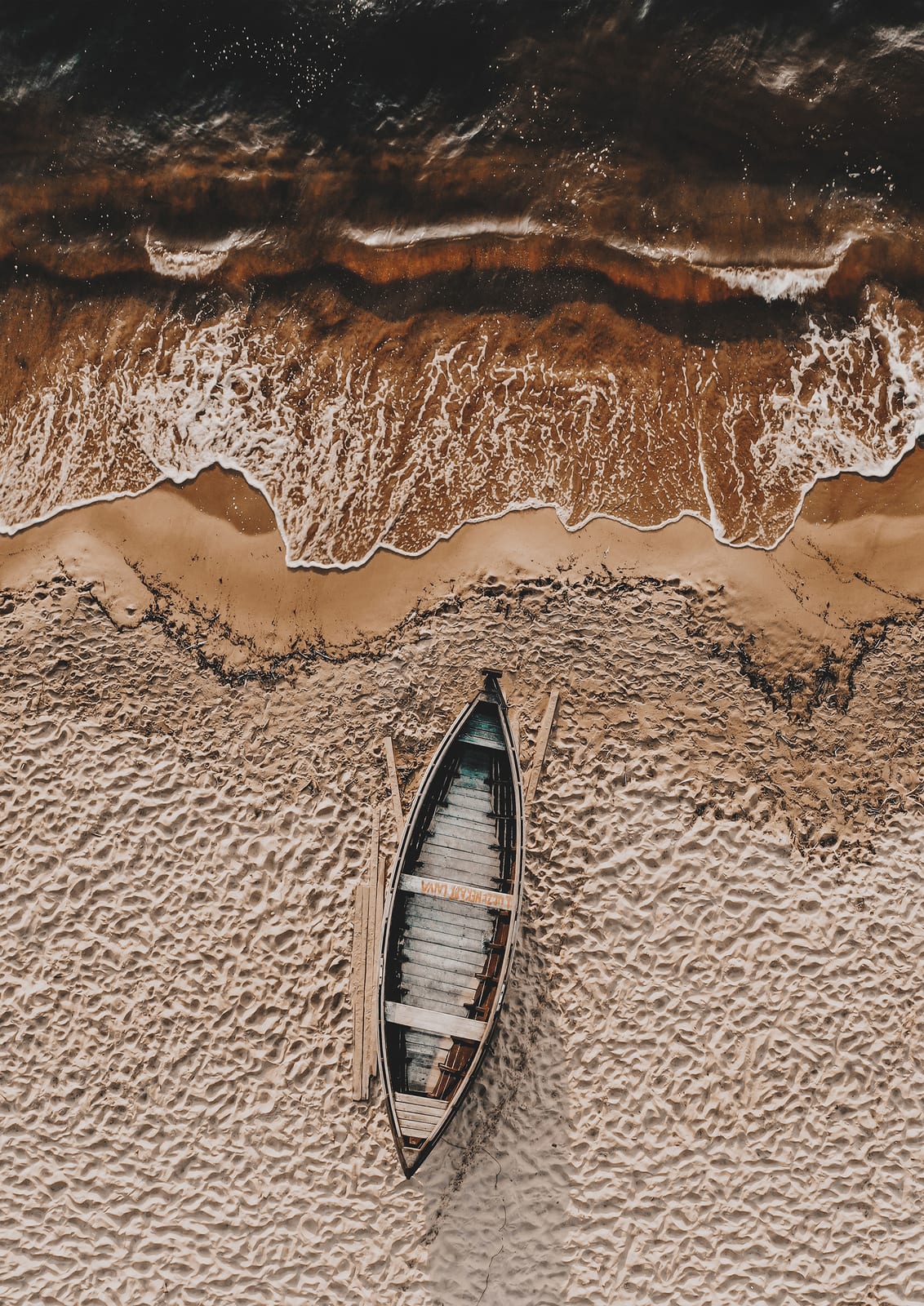 wooden boat on rippled sand beside a wave.