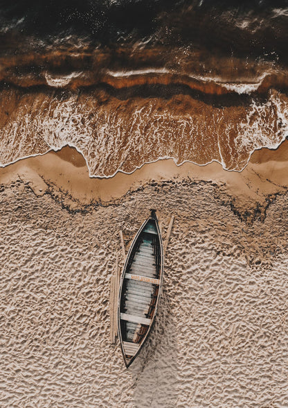 wooden boat on rippled sand beside a wave.
