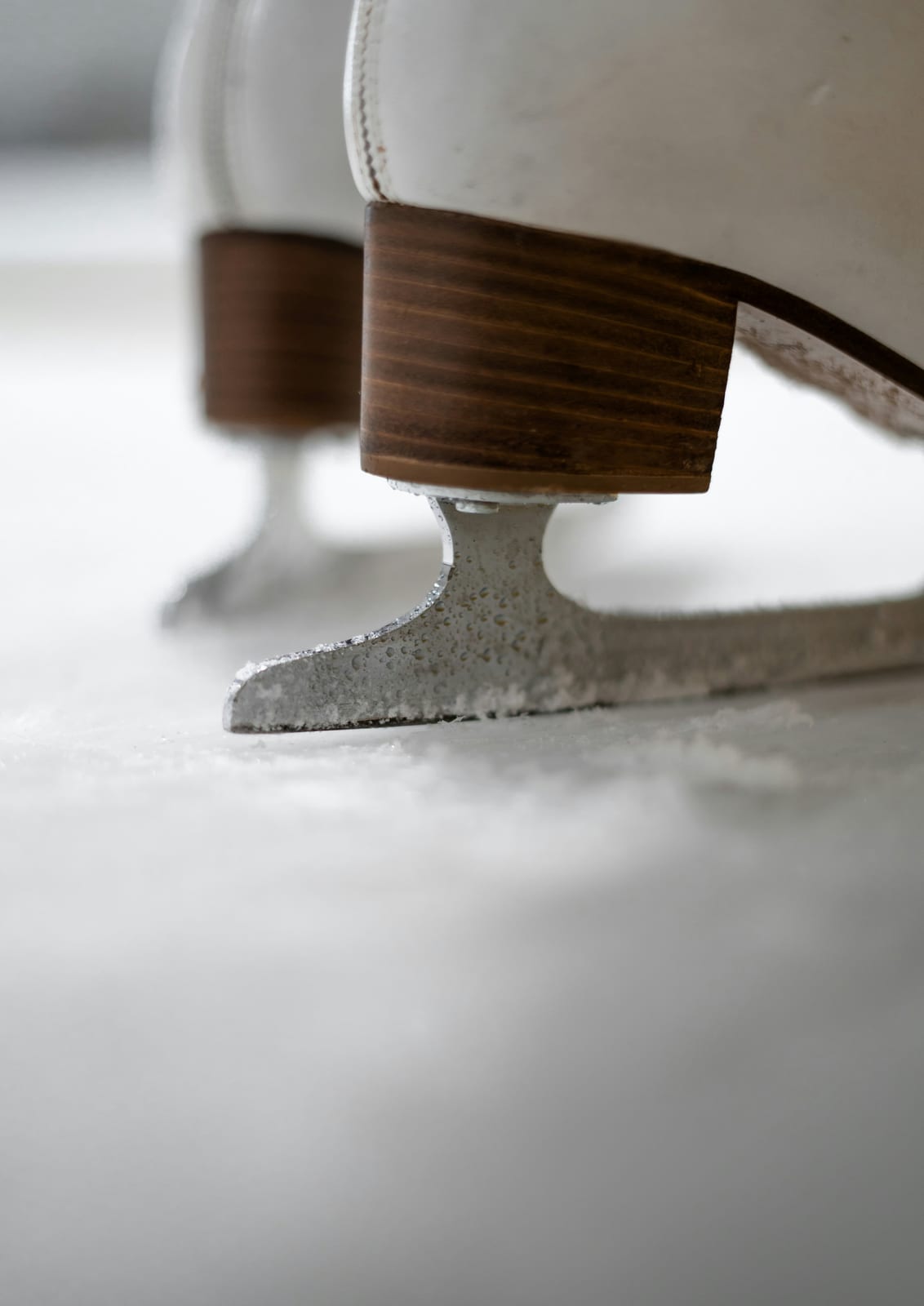 A white ice skate has a brown sole and metal blade.