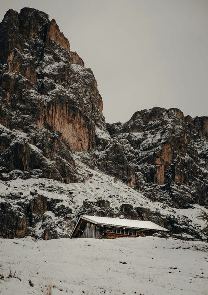 Snow-covered rocks rise behind a low wooden cabin.