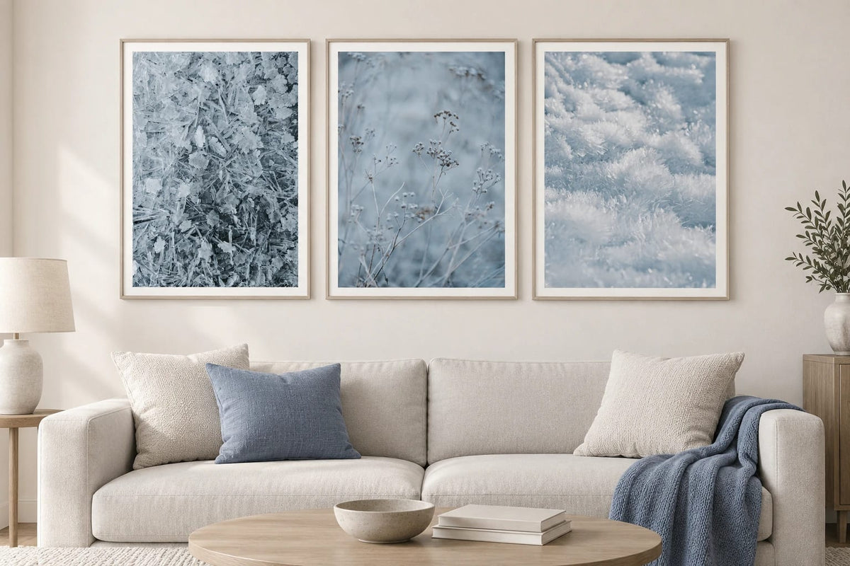 Three frost and snow prints hang above a light sofa with blue pillows.