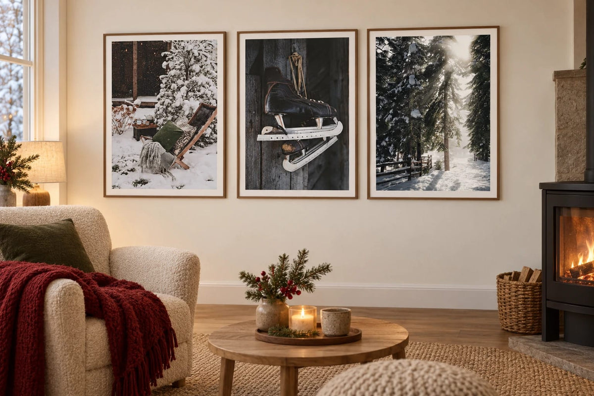 Three winter prints with a chair, skates, and forest hang near a fireplace.