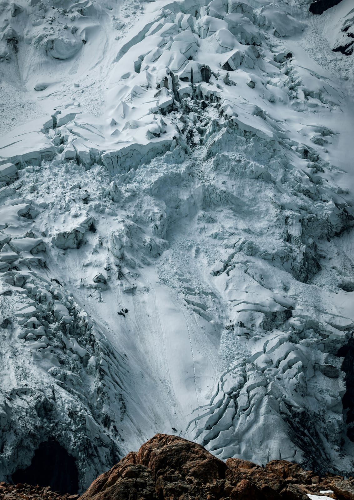 A blue-white icy cliff shows a brown stone edge.