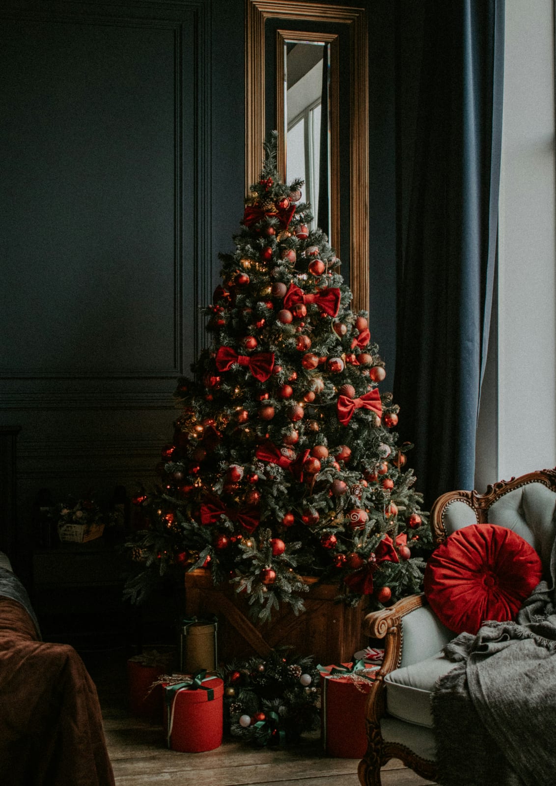 A Christmas tree is decorated with red and gold details in a dark room.