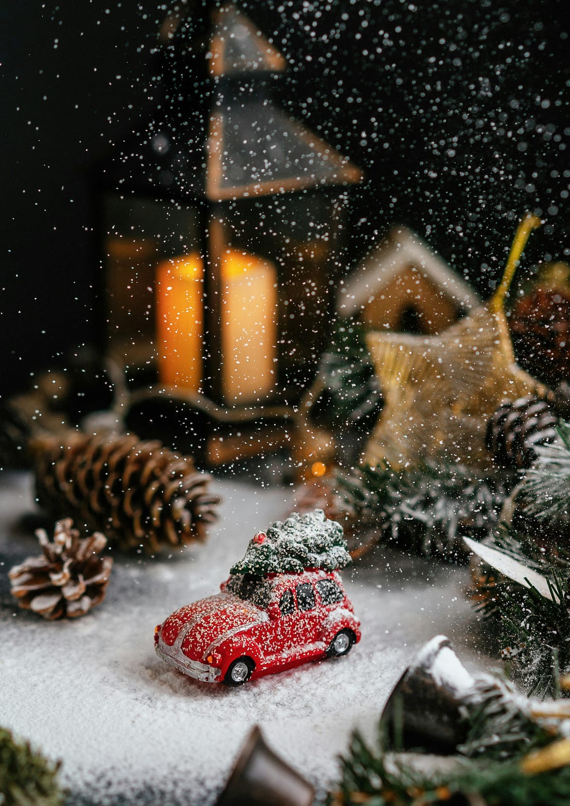 A red toy car carries a small tree across a snowy tabletop.