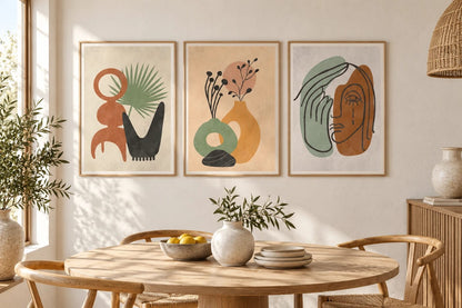 Three botanical prints hang above a round wood dining table near a window.
