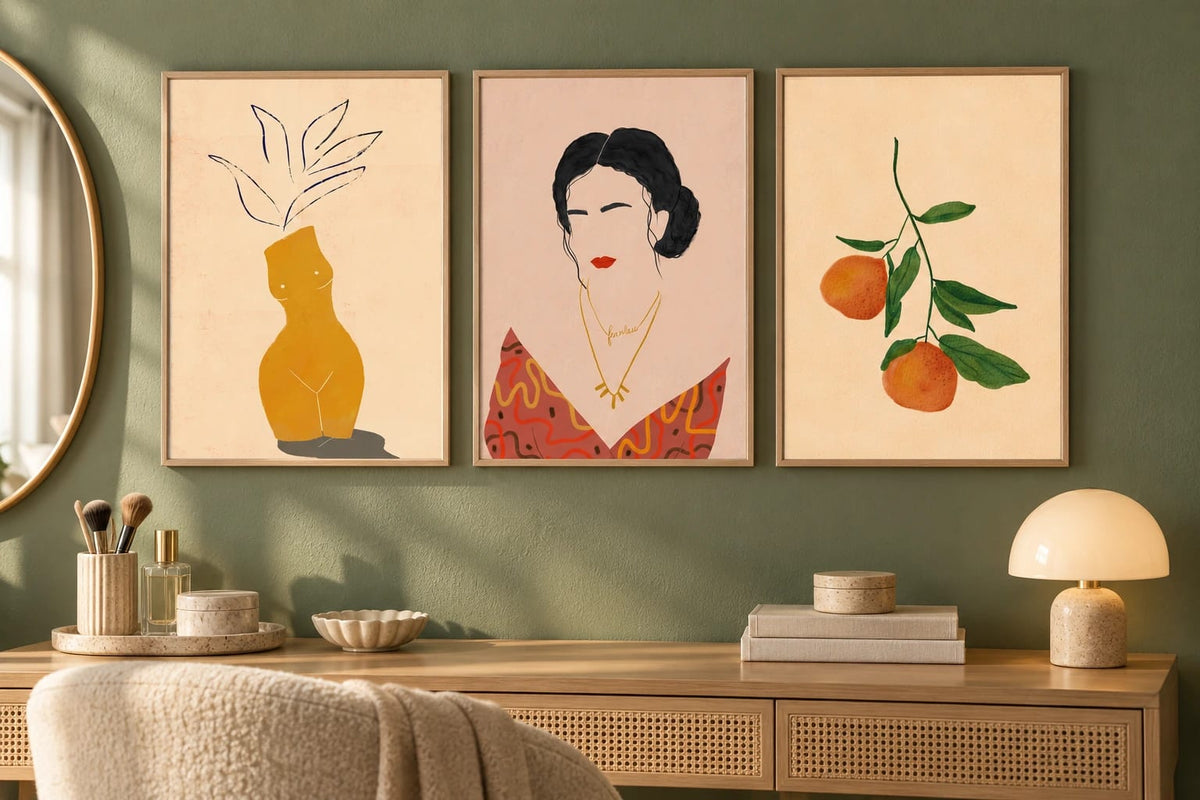 Three prints hang on an olive wall above a wood dresser with books and a lamp.