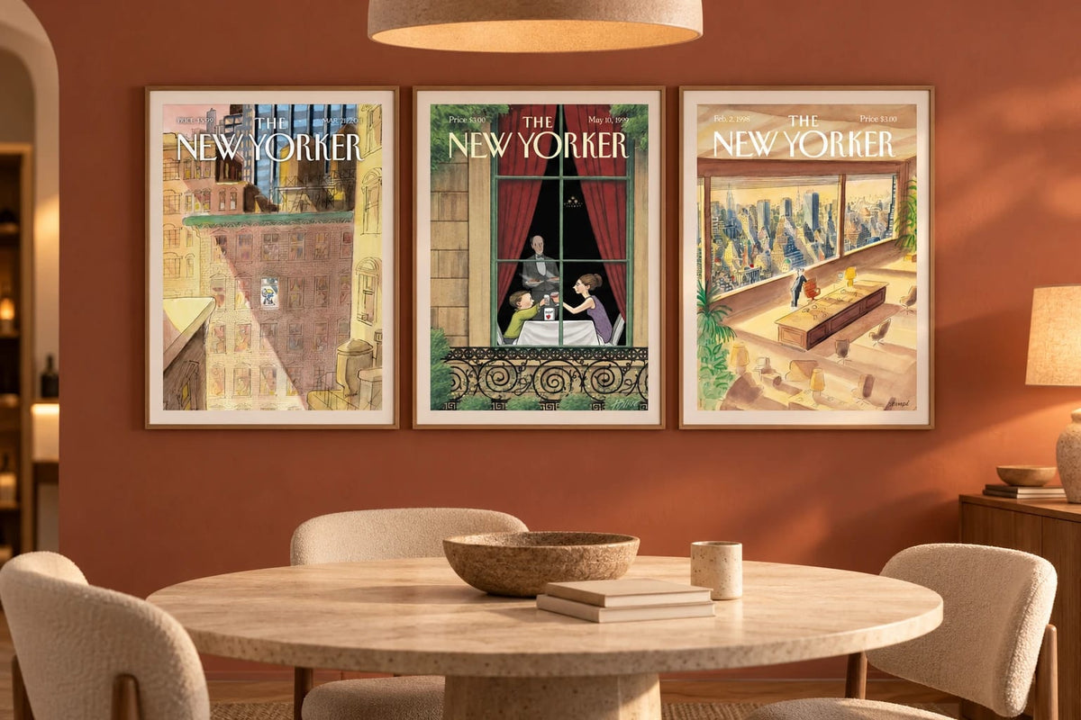 Three framed prints hang on a terracotta wall above a round dining table with light chairs.