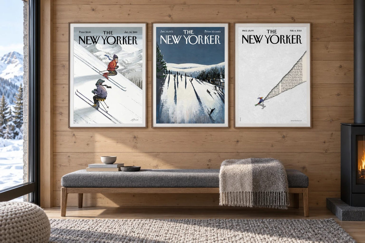 Three ski prints hang on a light wood wall above a long bench beside a window.