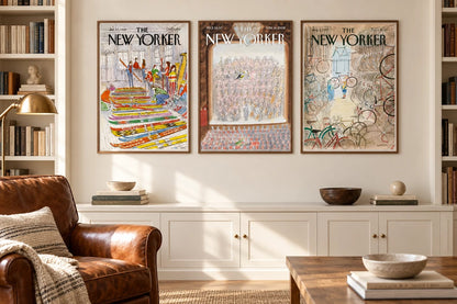 Three framed prints hang between bookshelves beside a leather chair and brass lamp.