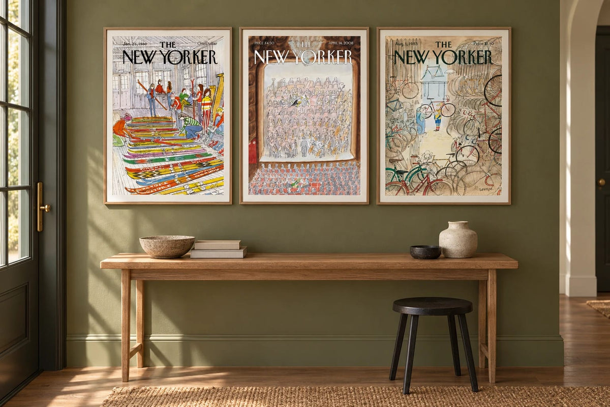 Three framed prints hang on an olive wall above a wood console beside a window.