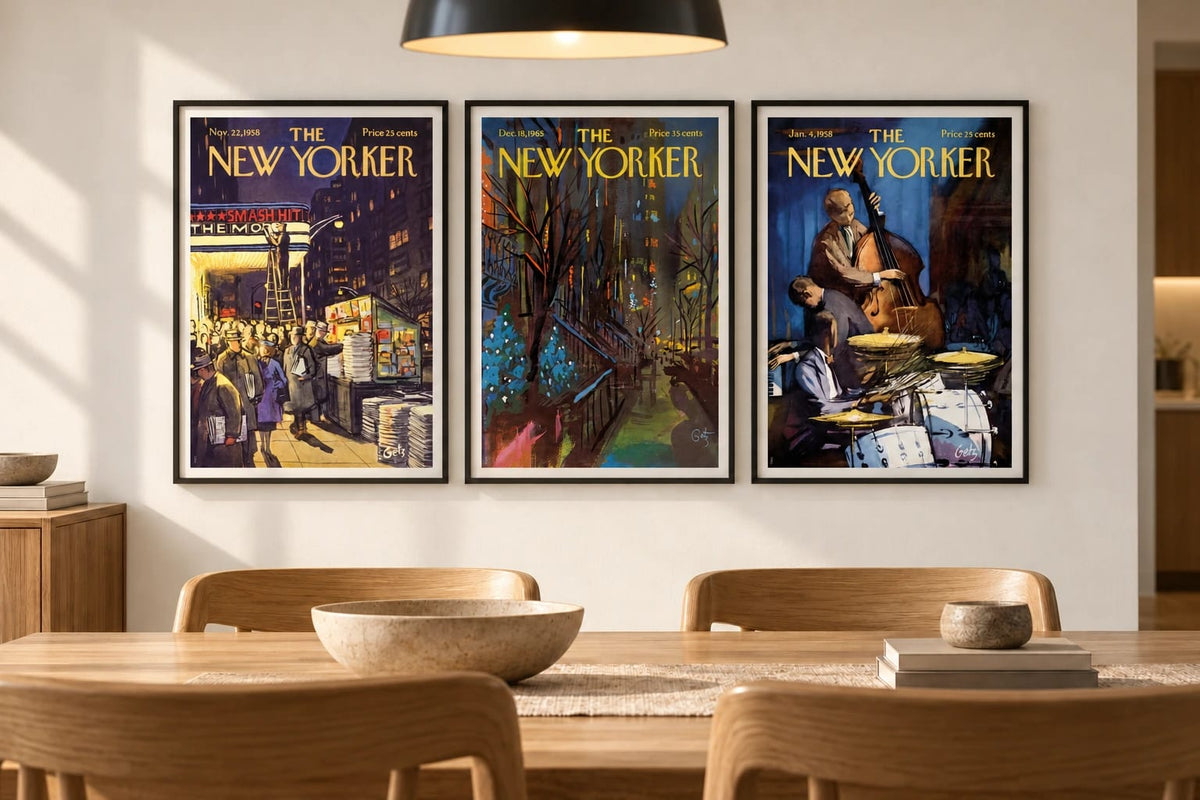Three framed prints hang on a light wall above a wood dining table beneath a black pendant light.