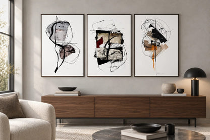 Three abstract prints hang above a walnut cabinet beside a cream chair in a light living room.